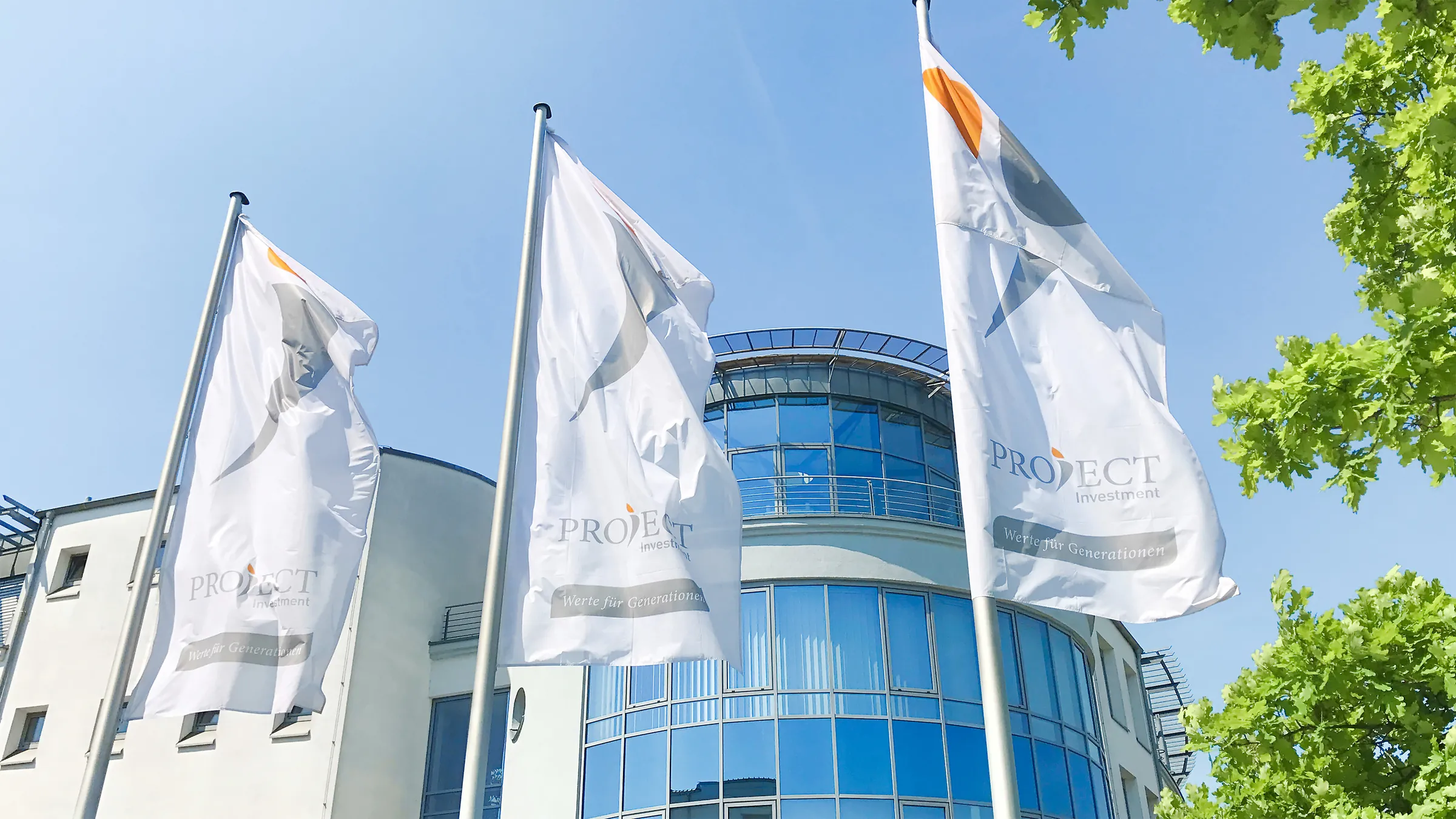 Drei weiße Fahnen mit dem PROJECT-Logo vor einem Bürogebäude mit Glasfassade, blauer Himmel